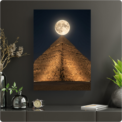Affiche verticale représentant la Grande Pyramide de Gizeh en Égypte, illuminée de bas en haut par des projecteurs, sous un ciel nocturne profond parsemé de quelques étoiles. Une pleine lune brillante et imposante est parfaitement centrée au-dessus de l'apex de la pyramide, créant une scène majestueuse et mystérieuse. Le sable du désert est visible au premier plan, accentuant l'immensité du monument.