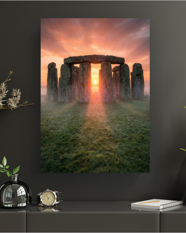 Affiche verticale de Stonehenge au lever du soleil. Les imposantes pierres grises du monument mégalithique sont baignées dans une lumière orange et rose intense émanant du soleil bas, perçant à travers les arches et la brume légère au sol. Le ciel est teinté de couleurs chaudes, contrastant avec l'herbe verte et humide au premier plan. L'ensemble dégage une atmosphère mystique et majestueuse.